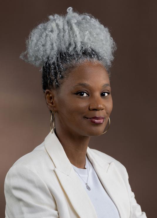 A photographic portrait of a Black woman smiling and looking at the camera. Un portrait photographique d’une femme noire qui sourit et regarde l’objectif.
