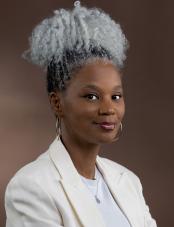 A photographic portrait of a Black woman smiling and looking at the camera. Un portrait photographique d’une femme noire qui sourit et regarde l’objectif.