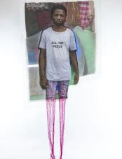 A print on white fabric features a Black man in a white T-shirt that reads “All the feels.” Magenta embroidery hangs at the bottom of the work. Une impression sur tissu blanc représente un homme noir portant un t-shirt blanc avec l'inscription « All the feels ». Des broderies magenta pendent au bas de l'œuvre.