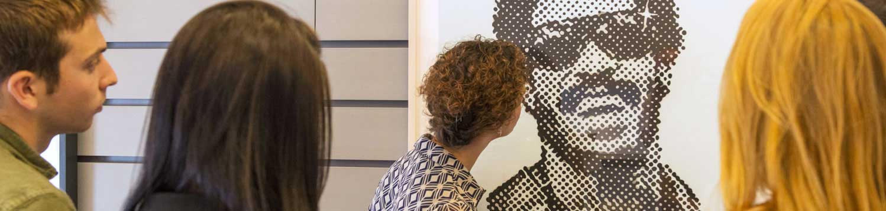 Students look closely at a pop art print that emphasizes the artifacts of half-tone printing.
