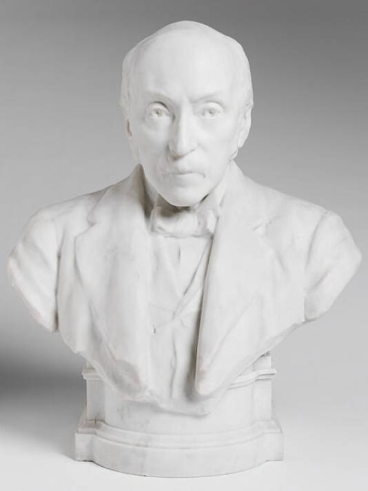 A bust in white marble of a man with closely cropped hair and beard, wearing a suit and bowtie.