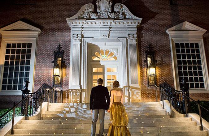 A couple standing at the bottom of a marble stairway looking up at the ornate door on the Quincy street entrance to the Harvard Art Museums
