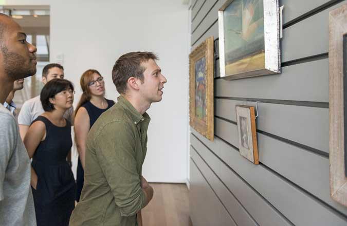 A group of students look closely at a painting in the art study center.